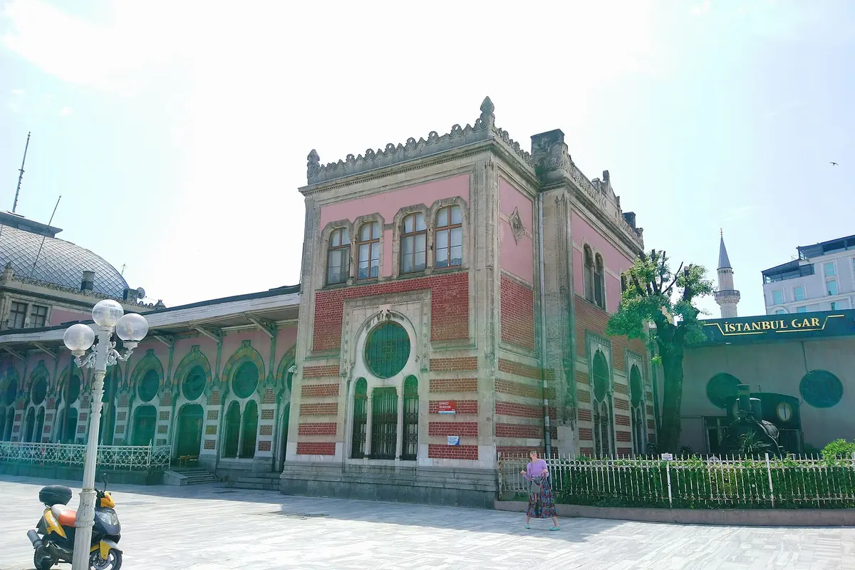 The pink and white brick facade of Sirkeci railway terminal across a paved square.